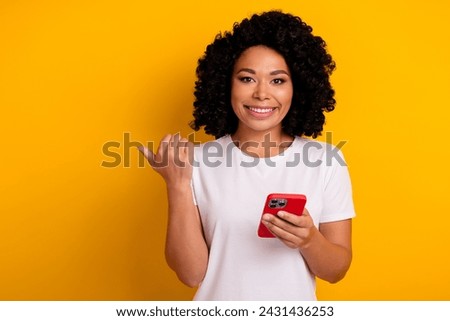 Photo of charming lovely woman with chevelure holding smartphone indicating at discount empty space isolated on yellow color background