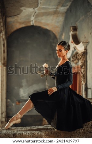 A gracious diva sitting in ruined building in her black dress with a rose in her hands. Side view of an elegant diva sitting in ruined and abandoned rustic place indoors with a flower in her hands. Royalty-Free Stock Photo #2431439797