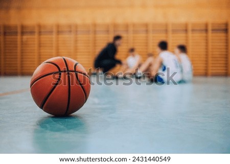 A basketball on court with a junior team with coach in a blurry background. A ball on basketball court during the training. A junior team with basketball coach in a blurry background. Copy space.