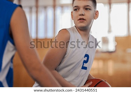 Dynamic portrait of a yong athlete guarding basketball on training at indoor court. A junior basketball player in action guarding a ball on basketball court during the training. Boy with basketball.
