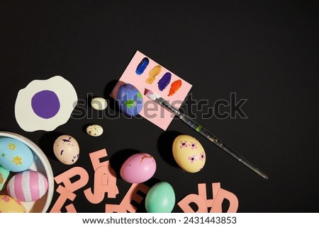 Black background featured Easter eggs painted with different patterns and colors. Some letters made of paper displayed with paintbrush and a paper of paint colors. Happy Easter Day content
