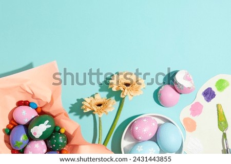 View from above of a vibrant collection of colorful painted striped Easter eggs decorated with candies, flower branches and a palette knife. Blue background. Copy space for banner or poster design