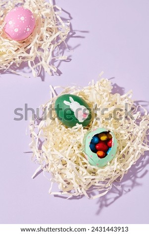 On purple background, paper cut into shreds form bird's nests with colorful eggs containing chocolate. Easter eggs have many meanings: fertility, proliferation and good luck