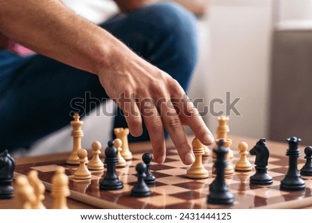 Chess match between friends. Hand of an unrecognizable man picking up one of the white pieces and placing it on the chessboard Royalty-Free Stock Photo #2431444125