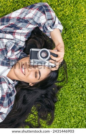 Aerial view of a smiling young woman lying on the grass taking photos with an analog camera