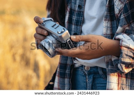Unrecognizable woman in checkered shirt and casual clothes taking photos with an analog camera in the field at sunset. The image conveys the concept of retro and vintage Royalty-Free Stock Photo #2431446923