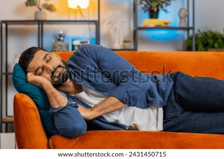 Bored young Indian man in casual clothes sleeping, enjoying carefree peaceful weekend relaxation on sofa at home. Hispanic guy lying on hands with pillow resting, lying asleep, feeling lack of energy.
