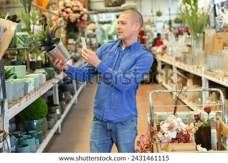 European man photographing artificial plant while making purchases in home goods store.