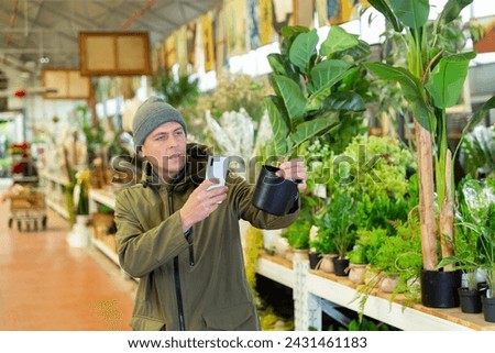 Caucasian man standing in salesroom of home goods store and photographing replica plant.