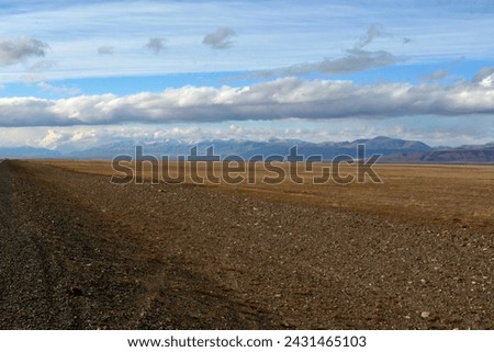 Flat boundless steppe with yellowed grass at the foot of a high mountain range under a cloudy autumn sky in the early evening.