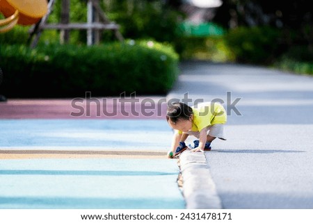 Portrait of Asian baby boy bending over to collect things, level floor, balance body, toddler learning in the world, relaxing time at the park, summer or spring time, one year old child.