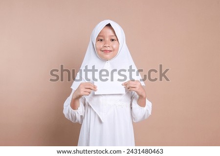 Asian Muslim little girl in hijab holding white envelope with happy expression