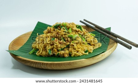 Mie Nyemek. Fried noodles served on a wooden plate lined with banana leaves with chopsticks on the side, on a white background