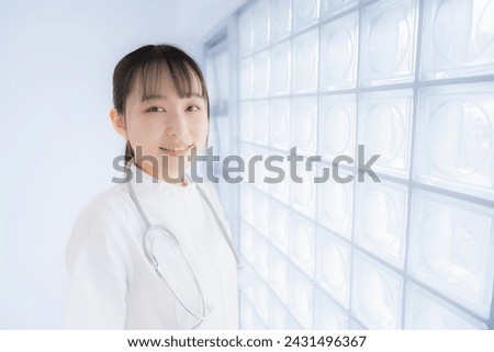 A Japanese female nurse smiles and poses by the window, looking at the camera.