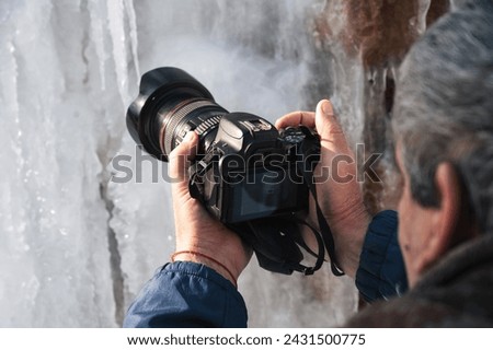 photographer's hand with a modern DSLR camera shoots icicles in winter in close-up