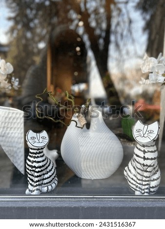 view of the window decorated with plaster figures of striped cats near a large vase with orchids on the windowsill.