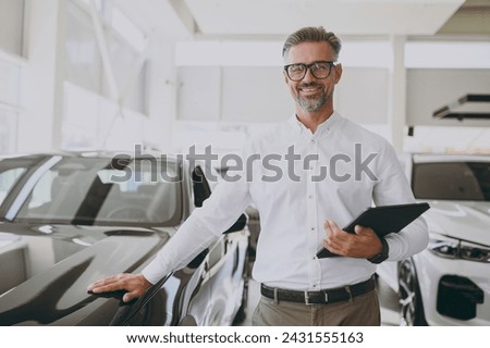 Adult man customer male buyer client wear shirt hold clipboard with contract documents choose auto want to buy new automobile in car showroom vehicle salon dealership store motor show. Sales concept