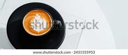 A cup of coffee with latte art in a black cup on white table background