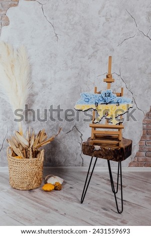 Wall clock in the shape of a map of Ukraine. On the easel. Ukrainian embroidery and coat of arms and flag of Ukraine. Clock hands and dial