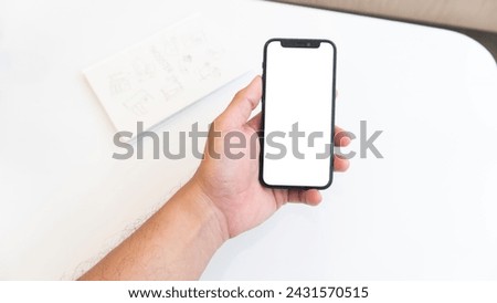 Close-up  image male using his smartphone at his office desk. smartphone white screen mockup, Man using smartphone blank screen frameless modern design while sitting on the chair in home interior.