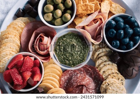 An artisanal, antipasto, fresh fruit, meat, and cracker grazing board finger food, with strawberries, blueberries, olives, ham, salami, chocolate and crackers. Royalty-Free Stock Photo #2431571099
