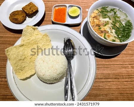Traditional Indonesian dish of clear chicken soup or soto ayam,served with white rice, crackers, lime slice, fried tempeh, rice vermicelli,chili sauce.It is popular in Singapore,Malaysia and Suriname.