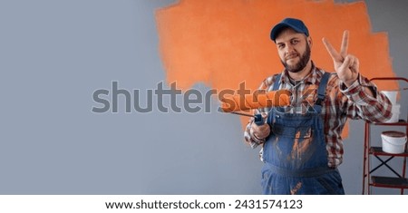 Painter man in overalls with painting roller smiling and showing victory sign. Banner. Copy space