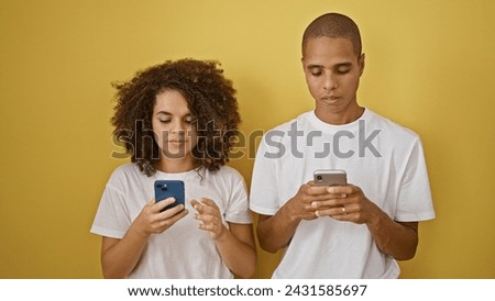 Beautiful couple using smartphones over isolated yellow background