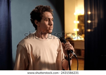 Young actor or showman speaking in microphone while looking at audience and pronouncing monologue on stage