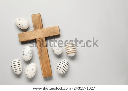 Wooden cross and painted Easter eggs on light grey background, flat lay. Space for text