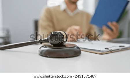 A focused man in a sweater reads a document in an office with gavel foreground emphasizing legal or judicial context. Royalty-Free Stock Photo #2431591489