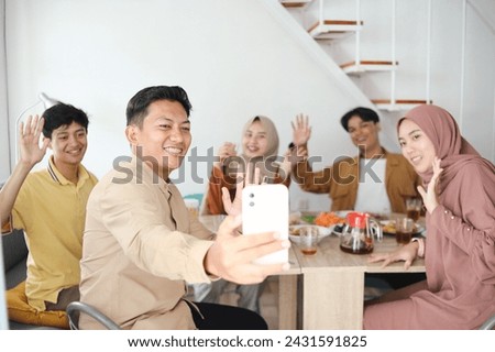 Asian muslim family having iftar dinner and making video call while eating traditional food during Ramadan month at home.