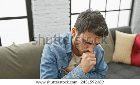 Hispanic man coughing in a modern living room, portraying illness Royalty-Free Stock Photo #2431592389