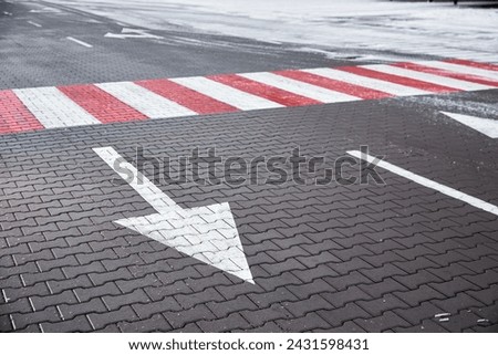 Road with a pedestrian crossing and arrows for traffic, in winter