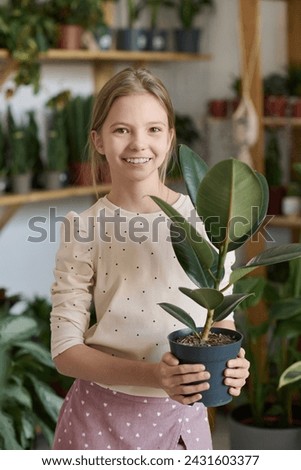 Vertical medium portrait of happy Caucasian girl holding houseplant smiling at camera