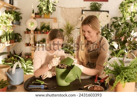Medium shot of Caucasian woman and her daughter standing at table taking care of houseplant