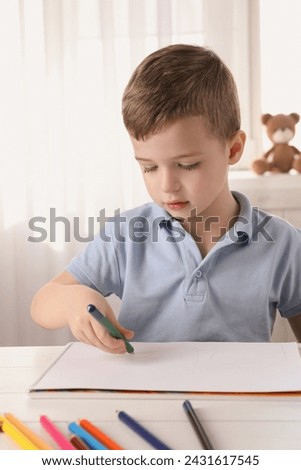 Cute little boy drawing with pencil at white table in room. Child`s art
