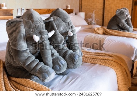 Three large gray plush elephant toys are sit on a hotel bed made of towel creating a warmth welcome family traveller and playful atmosphere in the luxury resort room Royalty-Free Stock Photo #2431625789