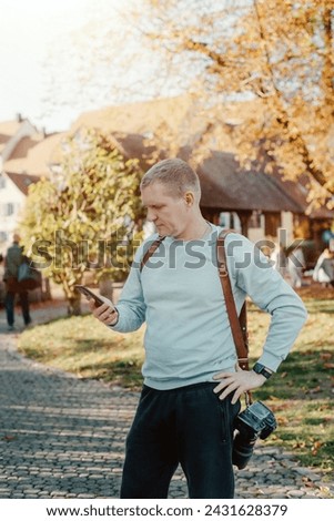 Professional Photographer Taking Picture Of Beautiful Autumn Park. Man Professional Photographer standing With Camera And With Smartphone In Autumn Park. Retouched, Vibrant Colors