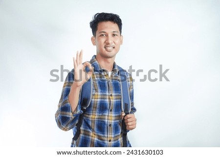 Smiling happy young Asian boy student wearing casual clothes and backpack showing ok sign, making approval gesture with finger isolated on white background. high school university college concept