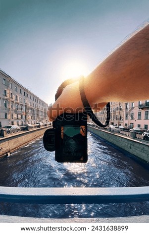 male hand holding a camera against the a river between old buildings to take a picture, pov, point of view perspective