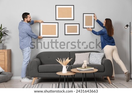 Man and woman hanging picture frames on gray wall at home