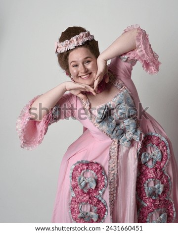 Close up portrait of cute female model wearing an opulent pink gown, the costume of a historical French baroque nobility, in style of Marie Antoinette with elegant hairstyle.
Isolated on studio backgr