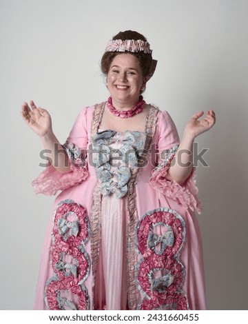 Close up portrait of cute female model wearing an opulent pink gown, the costume of a historical French baroque nobility, in style of Marie Antoinette with elegant hairstyle.
Isolated on studio backgr