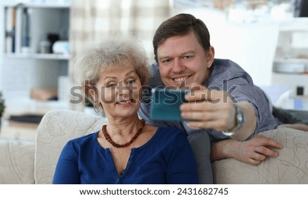 Portrait of cheerful mother and son taking selfie to remember. Smiling elderly woman posing for picture on sofa at home. Family relationship and spare time concept