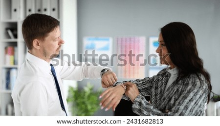 Portrait of business co-workers smiling and reconcile time on wristwatch. Brunette young woman and man in presentable suit in office. Company and time management concept Royalty-Free Stock Photo #2431682813