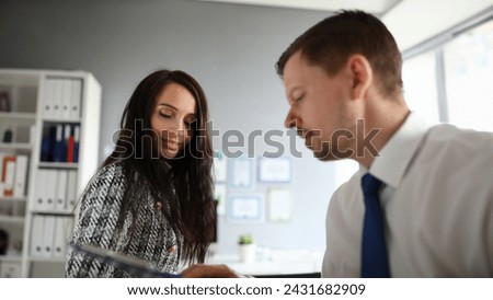 Close-up of smiling young female talking to co-worker and discussing working moment. Partners in presentable suits. Male employee in office. Business company concept Royalty-Free Stock Photo #2431682909
