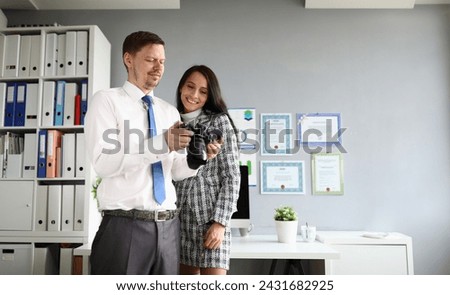 Portrait of smiling partners discussing working moments in office. Handsome male and attractive young woman in presentable suits. Company and photography concept Royalty-Free Stock Photo #2431682925