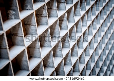 Close-up of a metallic grid with uniform square openings. The smooth metal and consistent pattern create a modern, industrial aesthetic.