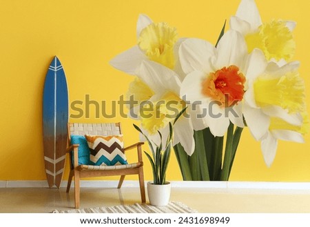 Stylish interior of room with armchair, surfing board and beautiful narcissus flower on wall